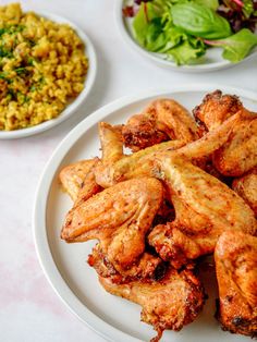 chicken wings on a plate next to a salad and rice