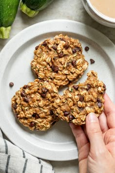 three cookies on a white plate with chocolate chips and avocado in the background