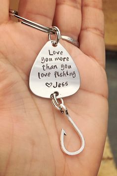 a hand holding a metal fishing hook with the words love you more than you love fishing