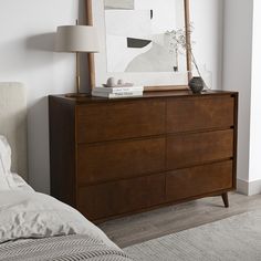 a bedroom scene with focus on the chest of drawers and a large framed art piece