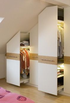 an attic bedroom with closets and clothes on the shelves in front of the bed