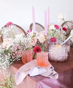 the table is set with candles, flowers and pink napkins on top of it