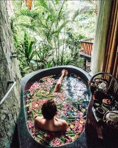 a man sitting in a bathtub filled with lots of colorful flowers and plants next to a window