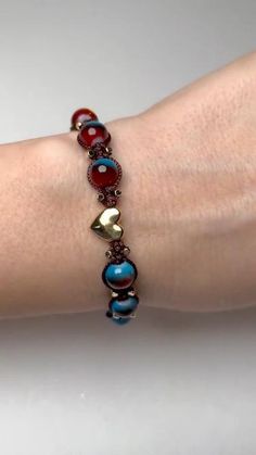 a woman's arm wearing a bracelet with red, blue and gold beads