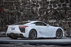 a white sports car parked in front of a stone wall with black rims on it