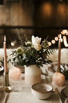 the table is set with candles, plates and flowers in white vases on it