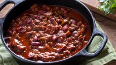 a pot filled with chili and meat on top of a wooden table