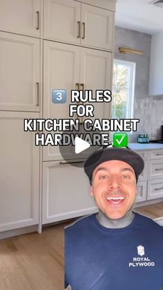 a man in a blue shirt and black hat standing in front of a kitchen with white cabinets