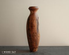 a tall wooden vase sitting on top of a cement floor next to a white wall