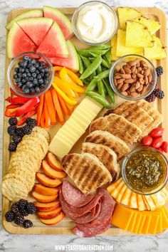 a platter filled with meats, fruit and veggies on a cutting board