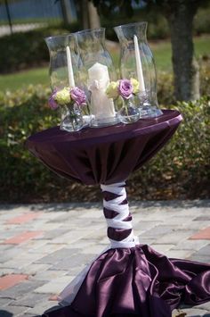 a table topped with two vases filled with flowers next to a purple satin skirt