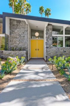 a yellow door sits in front of a stone house with palm trees and landscaping around it