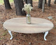 a vase with flowers sitting on top of a wooden table in the middle of a forest