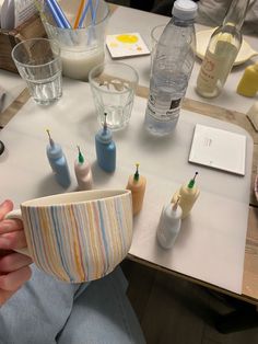 a person sitting at a table holding a cup with toothbrushes in it and other items on the table