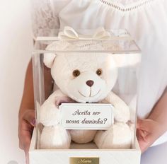 a person holding a white teddy bear in a clear box that says medita so nosa dominita?