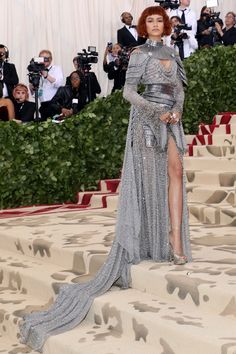 a woman in a silver dress standing on steps with cameras around her and people taking pictures