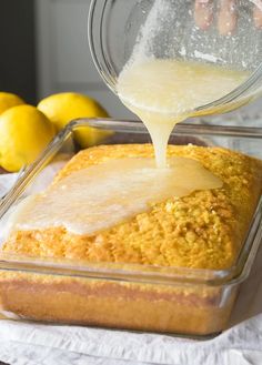 someone pouring batter on top of a loaf of bread in a glass pan with lemons behind it