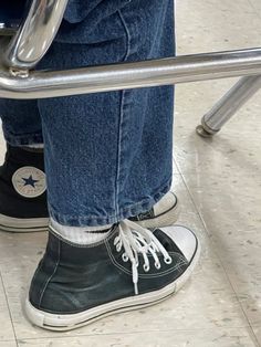 a person wearing black and white converse shoes standing in front of a metal rail with their legs crossed