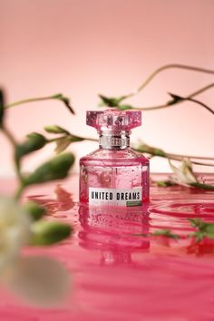 a pink perfume bottle sitting on top of a table next to flowers and water with the words united dreams written on it