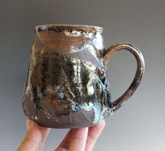 a hand holding up a brown and blue coffee cup with black glaze on it