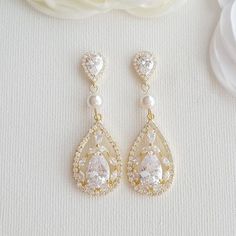 Delicate and elegant, the Esther gold wedding earrings are lovely drop earrings made with sparkling cubic zirconia in golden tones and accented with Swarovski pearls.I have created the bridal gold drop earrings with large cubic zirconia teardrops. The wedding earrings are dangled from 6mm Swarovski pearls and put onto cubic zirconia detailed halo set ear posts. All material is 14k gold plated brass with stainless steel posts. Also available in silver/rhodium plated brass and rose gold plated bra Gold Pearl Wedding Earrings, Gold Dangle Earrings Wedding, Expensive Earrings, Gold Wedding Earrings, Rose Gold Bridal Earrings, Gold Earrings Wedding, Bridal Earrings Drop, Gold Bridal Earrings, Wedding Earrings Drop