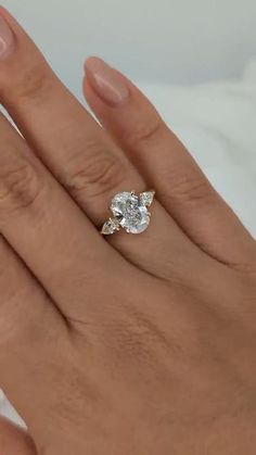 a woman's hand with a diamond ring on top of her finger and the other hand holding an engagement ring