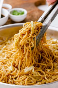 someone using tongs to eat noodles in a bowl with chopsticks on the side