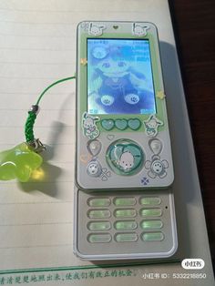 a cell phone sitting on top of a notebook next to a green string and an earphone