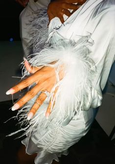 a woman with her hands on the arm of another person wearing white feathered dress