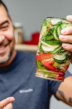 a man holding up a jar filled with lots of veggies and cucumbers