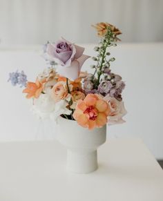 an arrangement of flowers in a white vase on a table with no one around it