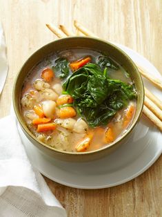 a bowl of soup with carrots, spinach and other vegetables on a plate