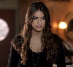 a woman with long brown hair wearing a black shirt and necklace standing in front of a mirror