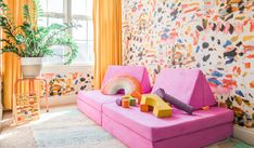 a living room with colorful furniture and wallpaper on the walls, including a pink couch