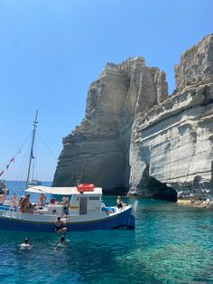 people are swimming in the blue water near a boat that is anchored at an island