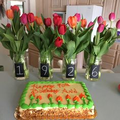 a birthday cake sitting on top of a table next to vases filled with flowers