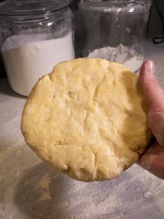 a person holding a cookie in their hand near some flour and glass jars on the counter