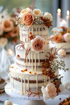 a three tiered wedding cake with flowers on top and candles in the back ground