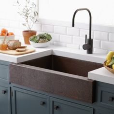 a kitchen sink sitting under a window next to a counter top with fruit on it