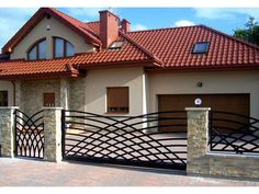 a house with an iron gate and brick driveway in the foreground, on a sunny day