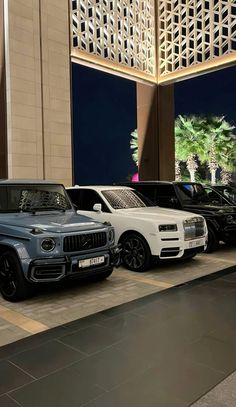 several cars are parked in front of a tall building at night with palm trees on the other side