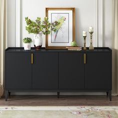 a sideboard with plants and candles on it in front of a framed painting, next to a rug