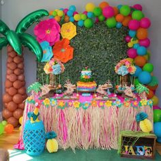 a table topped with lots of colorful balloons and desserts next to a palm tree