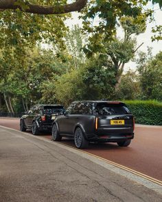 two cars are parked on the side of the road in front of some bushes and trees