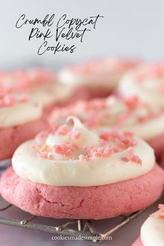 pink velvet cookies with white frosting and sprinkles on a cooling rack