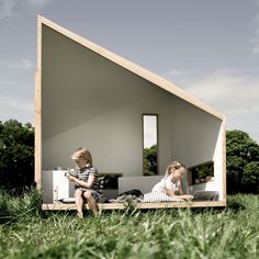 two children are sitting outside in front of a small house that's shaped like a boat