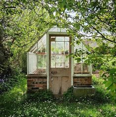 an old outhouse in the middle of some trees and grass with flowers around it