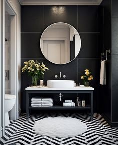 a black and white bathroom with a round mirror above the sink, rug on the floor