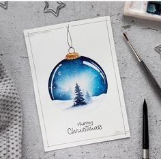 a christmas ornament is hanging on a card next to some paintbrushes