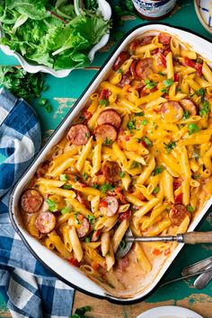 a casserole dish filled with sausage, pasta and cheese on a blue table